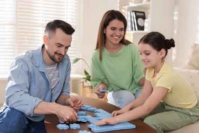 Happy parents and their daughter solving puzzle together at wooden table indoors