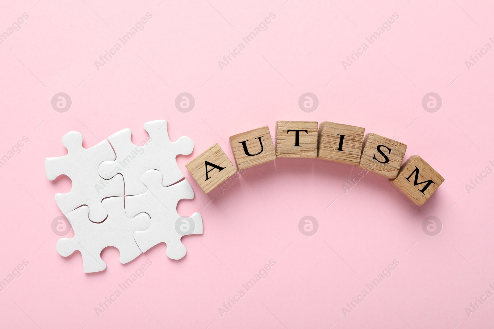 Photo of Word Autism made with wooden cubes and puzzle pieces on pink background, flat lay