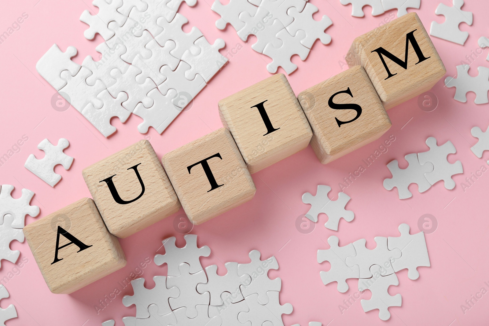 Photo of Word Autism made with wooden cubes and puzzle pieces on pink background, flat lay