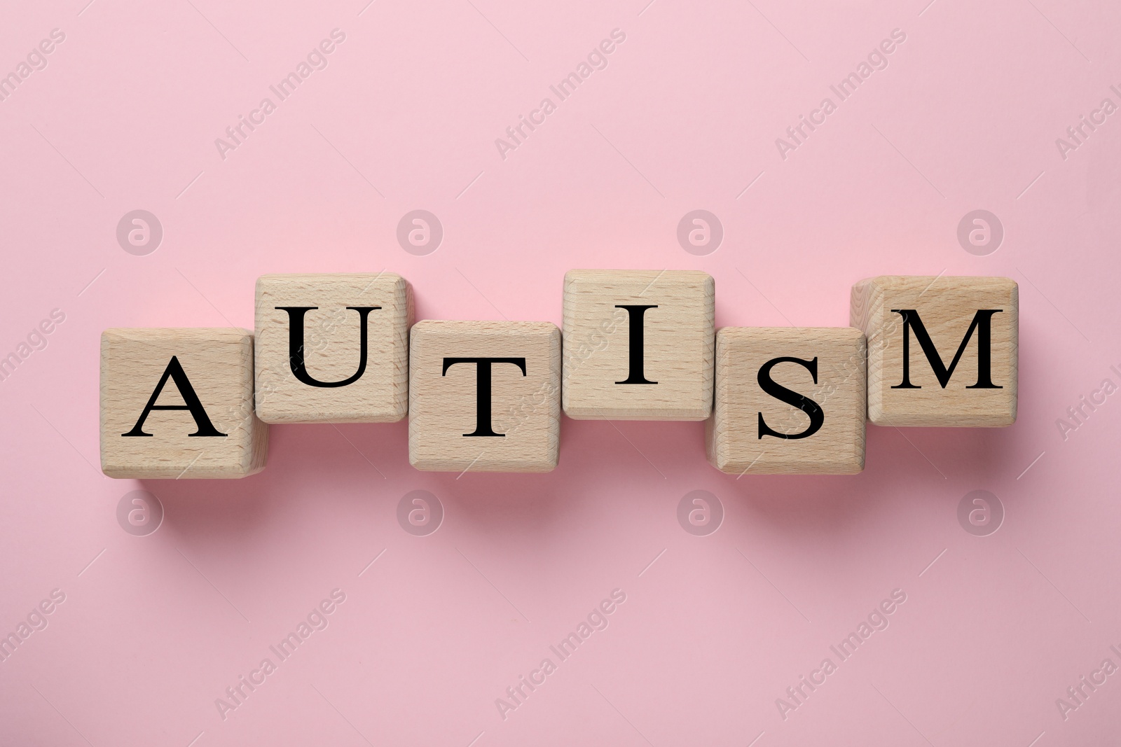 Photo of Word Autism made with wooden cubes on pink background, flat lay