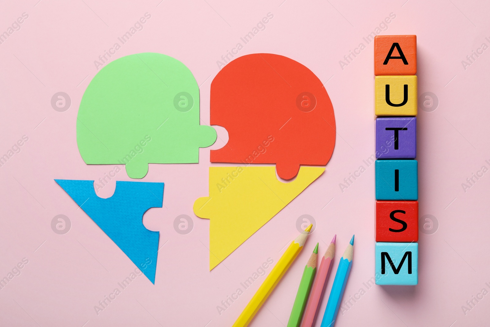 Photo of Colorful cubes with word Autism, pencils and heart made of puzzle pieces on pink background, flat lay