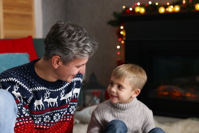 Photo of Dad and son near decorated fireplace at home. Christmas season