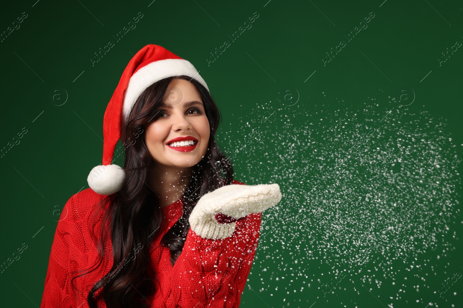 Photo of Attractive woman in Santa hat blowing snow off hands on green background. Christmas celebration