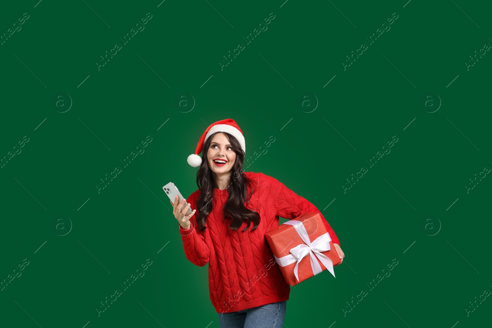 Photo of Attractive woman in Santa hat with Christmas gift and smartphone on green background