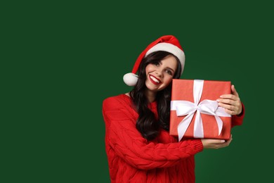 Photo of Attractive woman in Santa hat with Christmas gift on green background, space for text