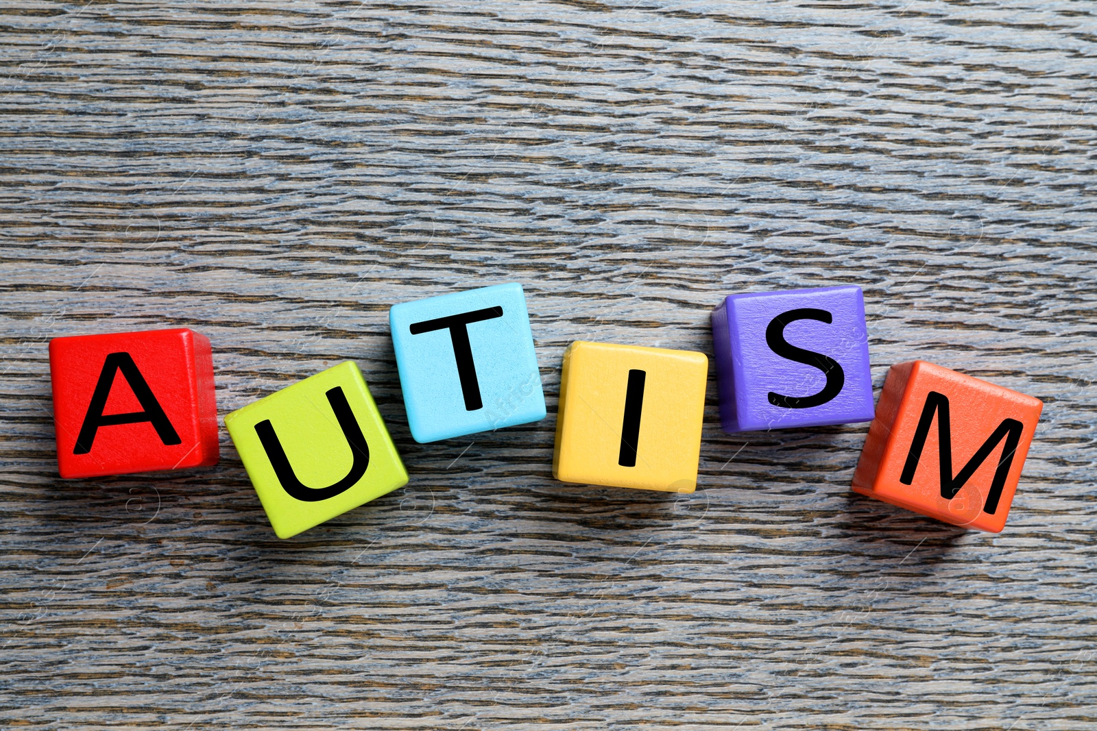 Photo of Word Autism made of colorful cubes on wooden background, top view