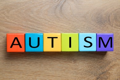 Photo of Word Autism made of colorful cubes on wooden background, top view