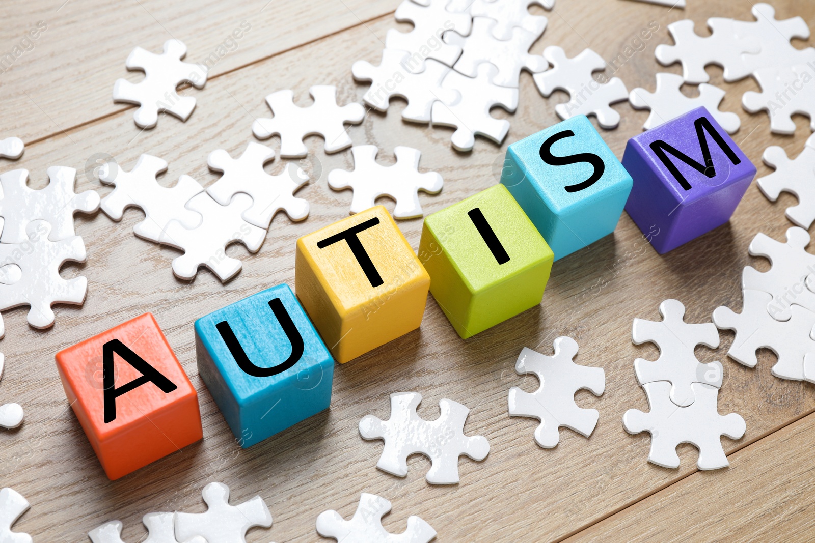 Photo of Word Autism made of colorful cubes and puzzle pieces wooden background