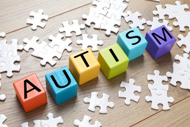 Photo of Word Autism made of colorful cubes and puzzle pieces wooden background