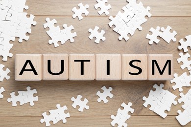 Photo of Word Autism made of cubes and puzzle pieces wooden background, flat lay