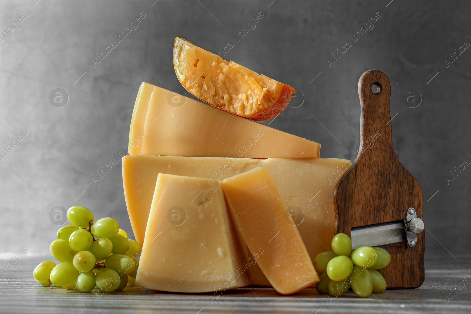 Photo of Different types of cheese, slicer and grapes on grey table