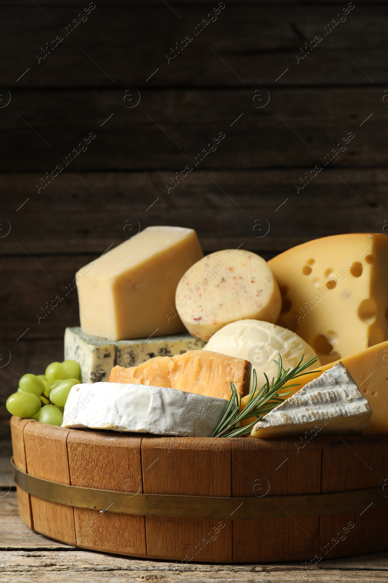 Photo of Different types of cheese, rosemary and grapes on wooden table