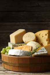 Photo of Different types of cheese, rosemary and grapes on wooden table