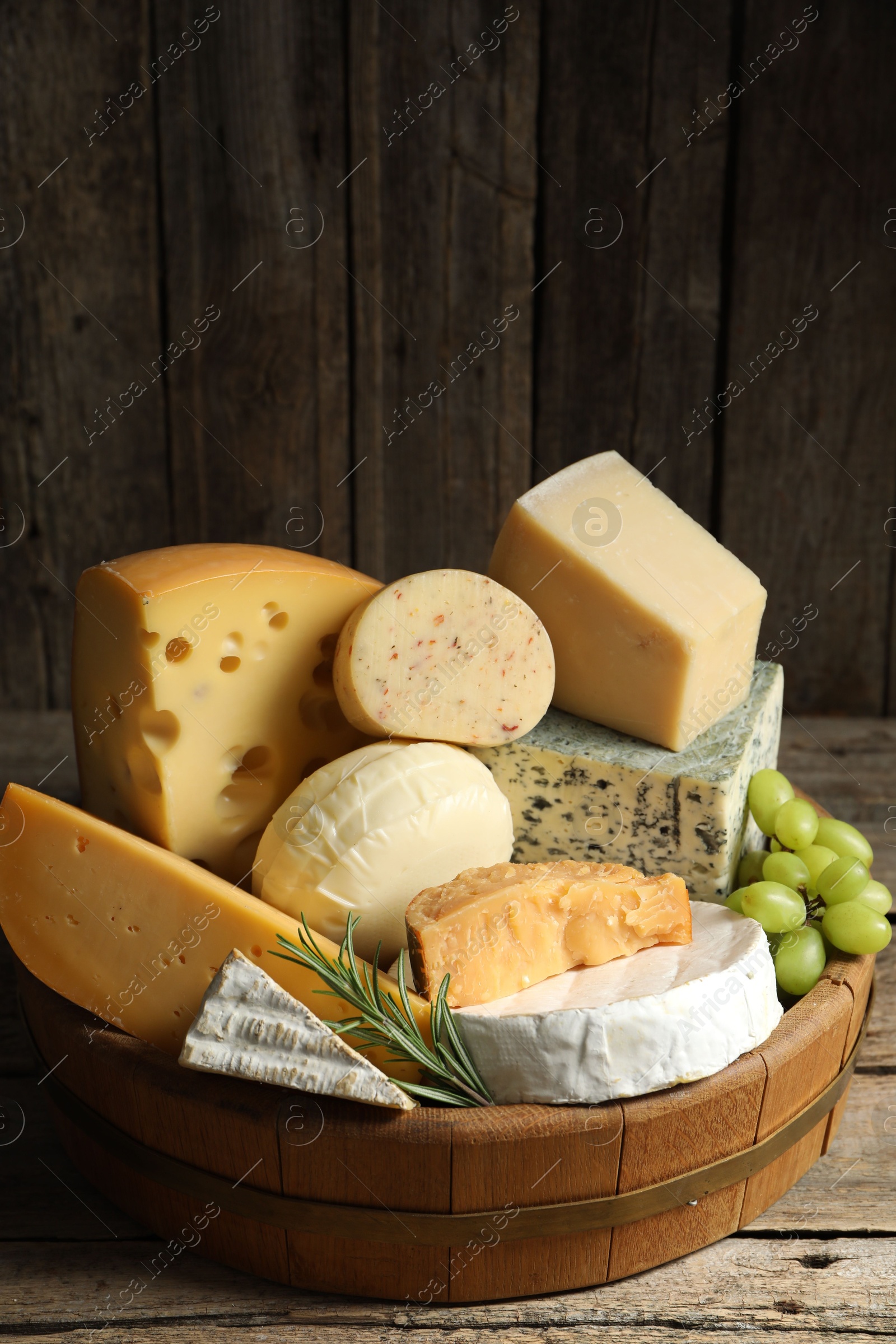 Photo of Different types of cheese, rosemary and grapes on wooden table