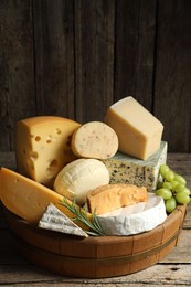 Photo of Different types of cheese, rosemary and grapes on wooden table