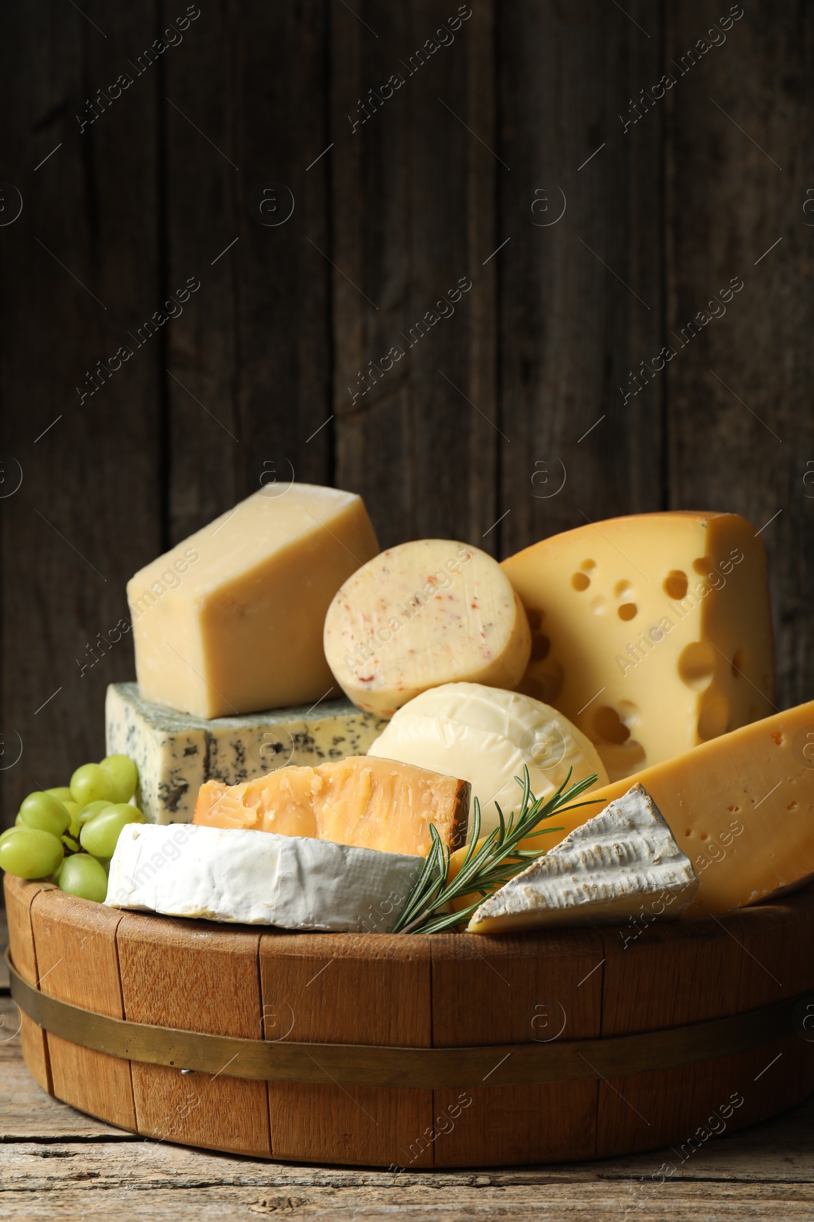 Photo of Different types of cheese, rosemary and grapes on wooden table