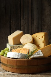 Photo of Different types of cheese, rosemary and grapes on wooden table