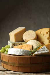 Photo of Different types of cheese, rosemary and grapes on wooden table, closeup