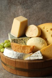 Photo of Different types of cheese and grapes in wooden tray on grey table, closeup