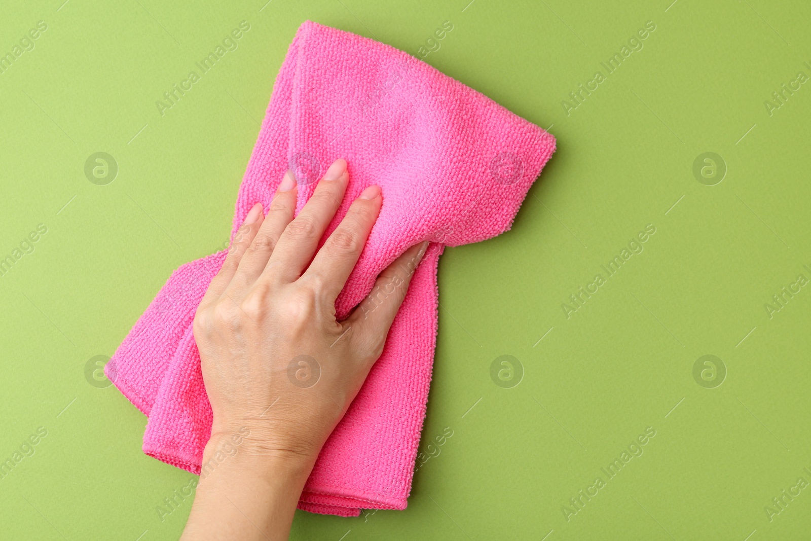 Photo of Woman with clean pink microfiber cloth on green background, top view. Space for text