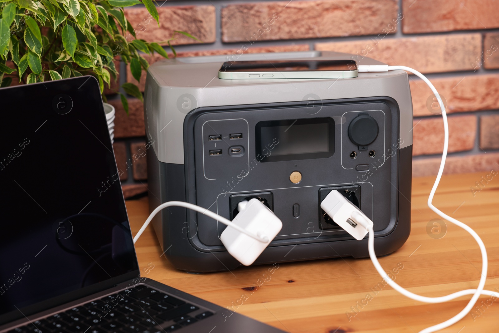 Photo of Devices charging from portable power station on wooden desk indoors