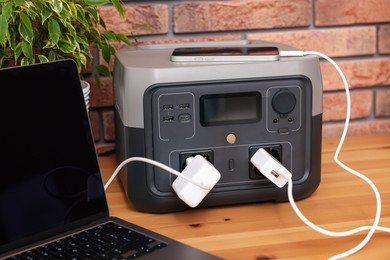 Photo of Devices charging from portable power station on wooden desk indoors