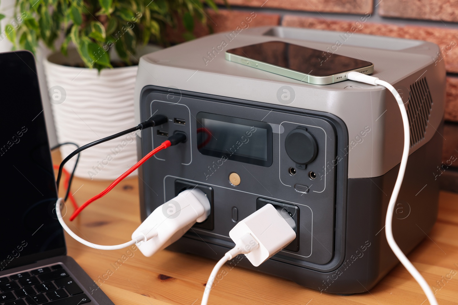 Photo of Devices charging from portable power station on wooden desk indoors