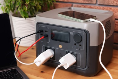 Photo of Devices charging from portable power station on wooden desk indoors