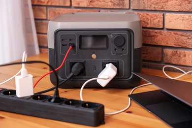 Photo of Laptop charging from portable power station on wooden desk indoors