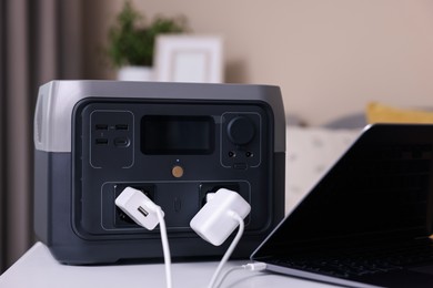 Photo of Laptop charging from portable power station on white table indoors