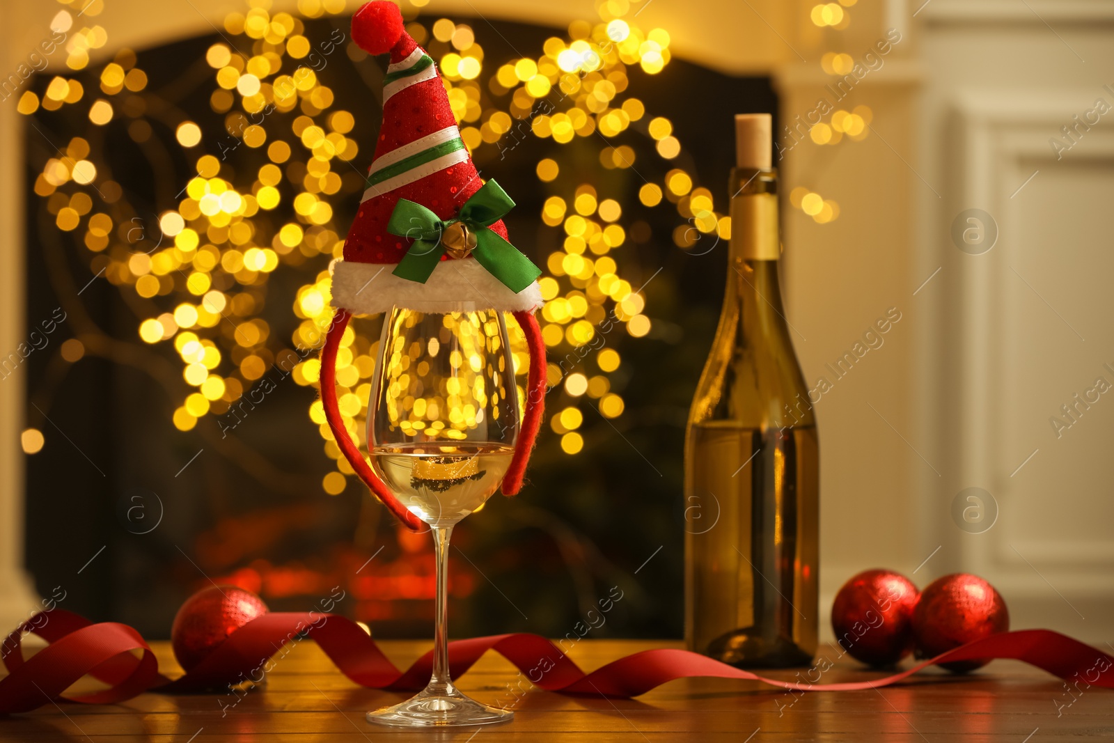 Photo of Glass of white wine and Christmas decor on wooden table against blurred lights. Bokeh effect