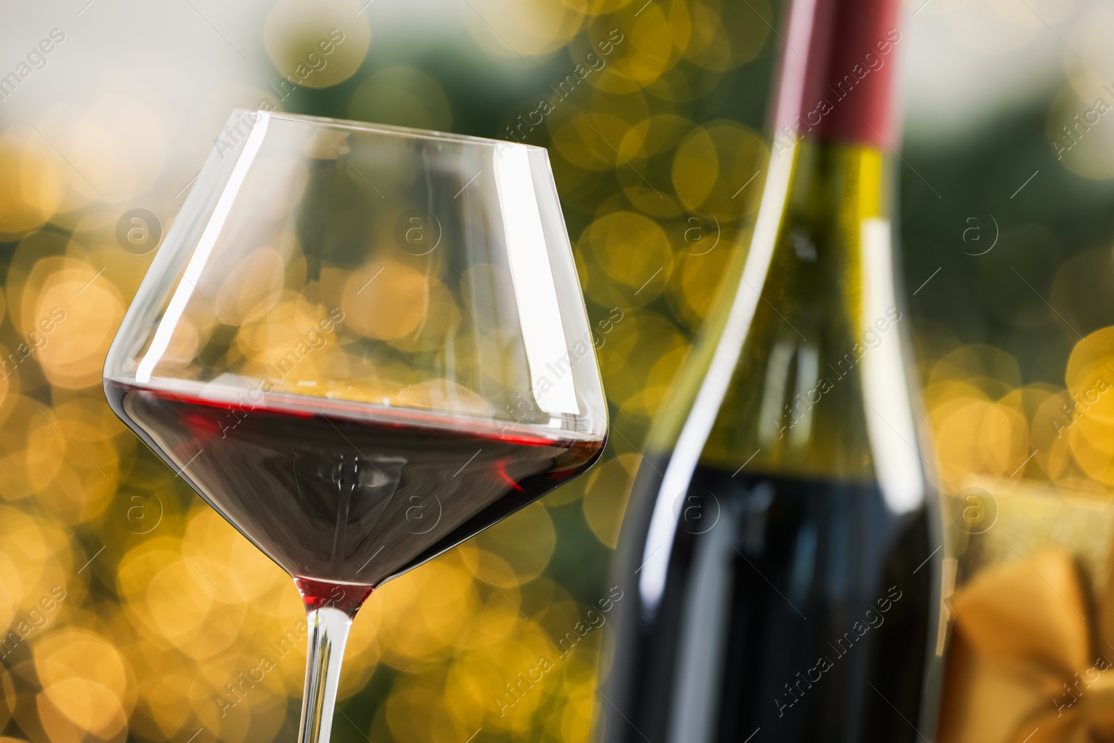 Photo of Glass and bottle of red wine against blurred Christmas lights, closeup. Bokeh effect