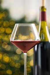 Photo of Glass and bottle of red wine against blurred Christmas lights, closeup. Bokeh effect