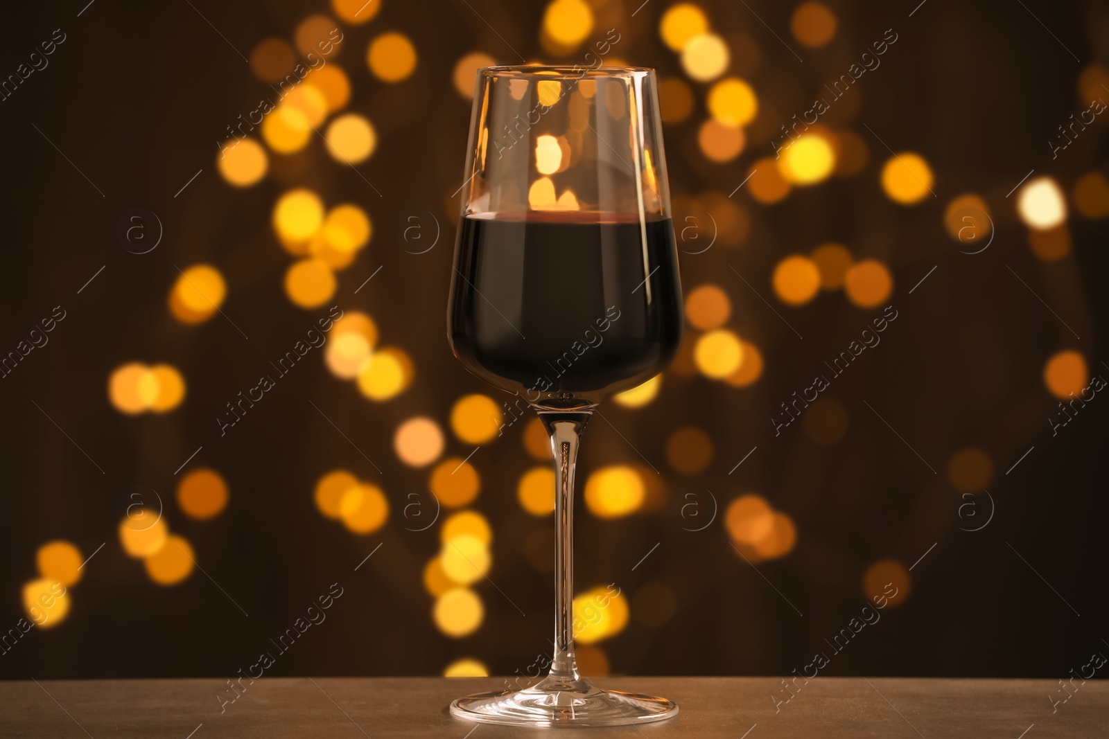 Photo of Glass of luxury red wine on wooden table against dark background with blurred lights. Bokeh effect