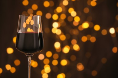 Photo of Glass of luxury red wine against dark background with blurred lights, closeup. Bokeh effect