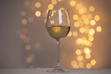 Tasty white wine in glass on table against grey background with blurred lights, bokeh effect