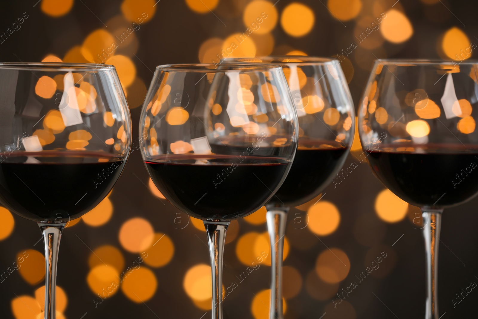 Photo of Tasty red wine in glasses against dark background with blurred lights, closeup. Bokeh effect