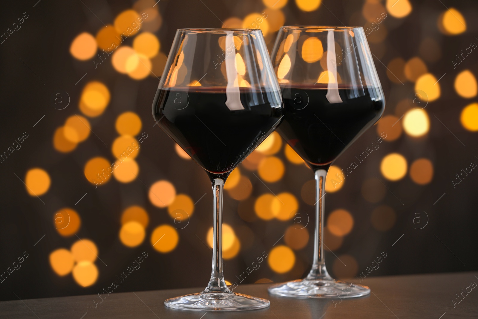 Photo of Tasty red wine in glasses on table against dark background with blurred lights, bokeh effect