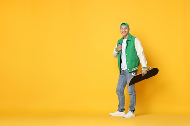 Photo of Happy man with skateboard on orange background. Space for text