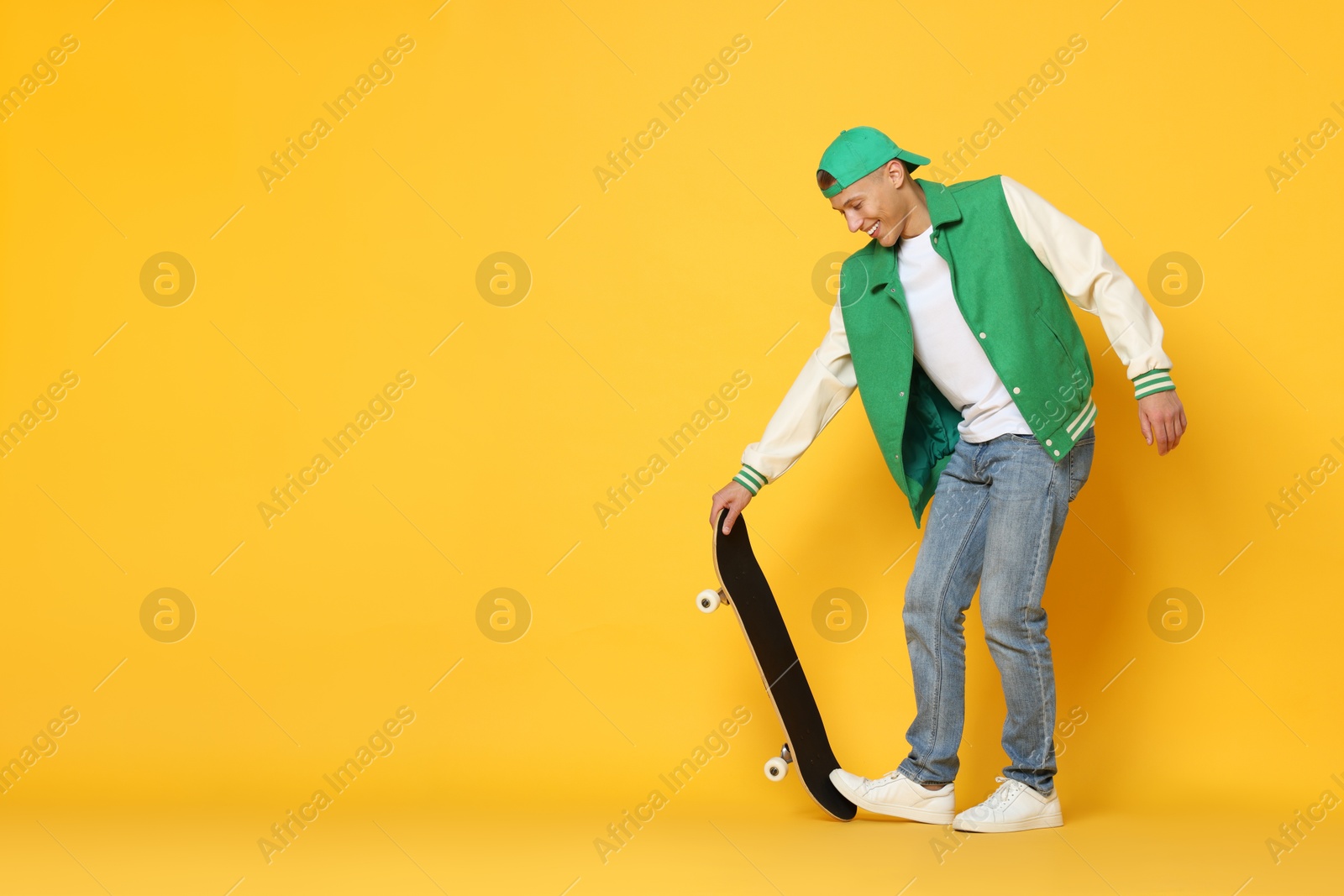 Photo of Happy man with skateboard on orange background. Space for text