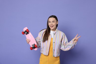 Photo of Smiling woman with penny board showing peace sign on violet background