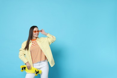 Photo of Smiling woman with penny board on light blue background. Space for text