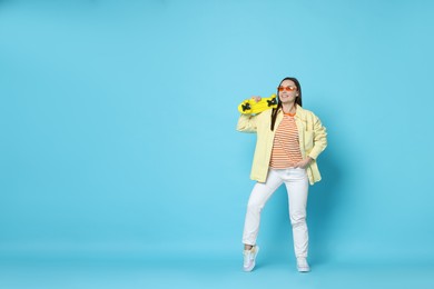 Photo of Smiling woman with penny board on light blue background. Space for text