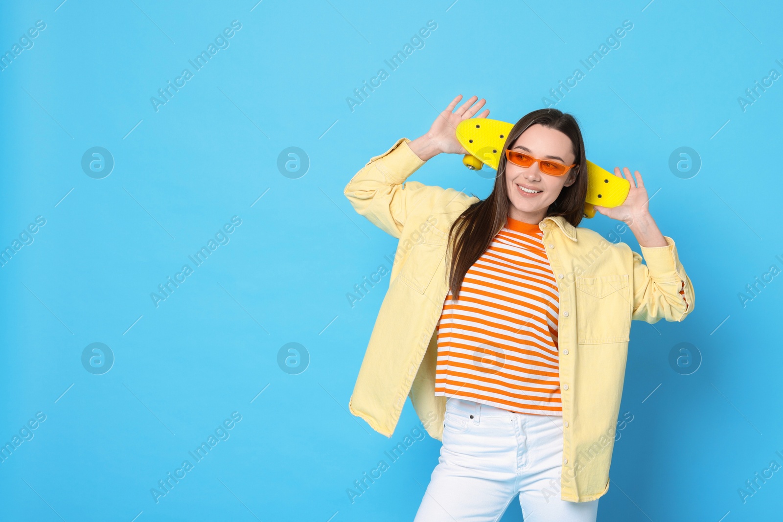 Photo of Smiling woman with penny board on light blue background. Space for text