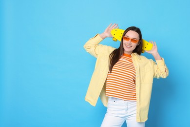 Photo of Smiling woman with penny board on light blue background. Space for text