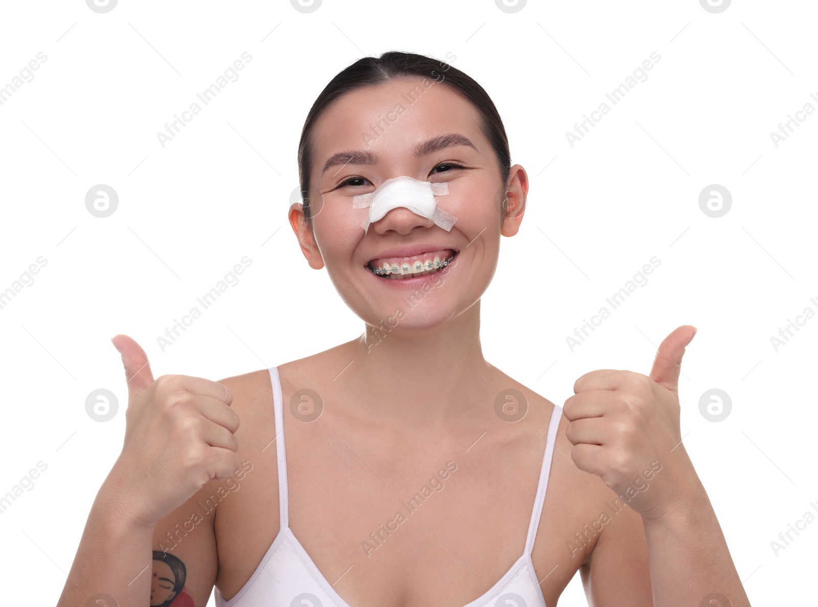 Photo of Woman with medical bandage on her nose after plastic surgery operation showing thumbs up against white background