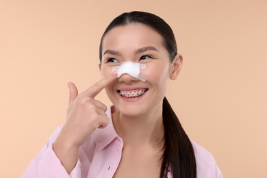 Photo of Woman with medical bandage on her nose after plastic surgery operation against beige background