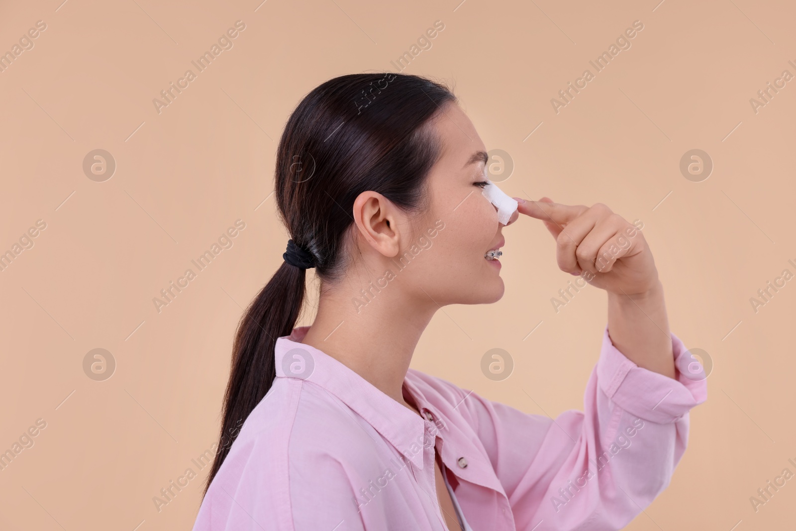 Photo of Woman with medical bandage on her nose after plastic surgery operation against beige background