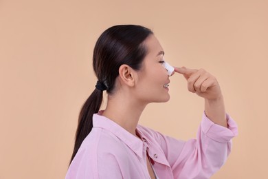 Woman with medical bandage on her nose after plastic surgery operation against beige background