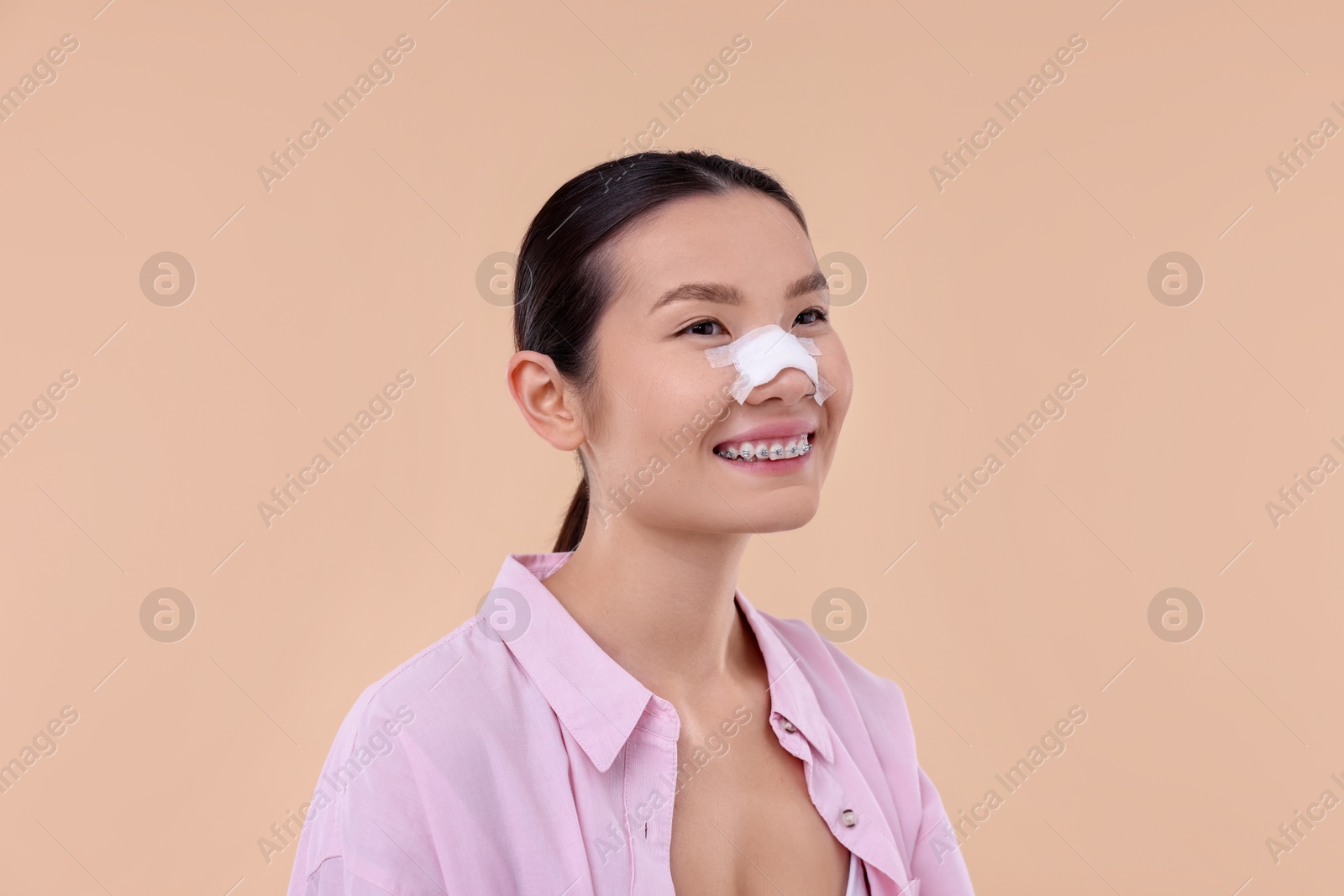 Photo of Woman with medical bandage on her nose after plastic surgery operation against beige background